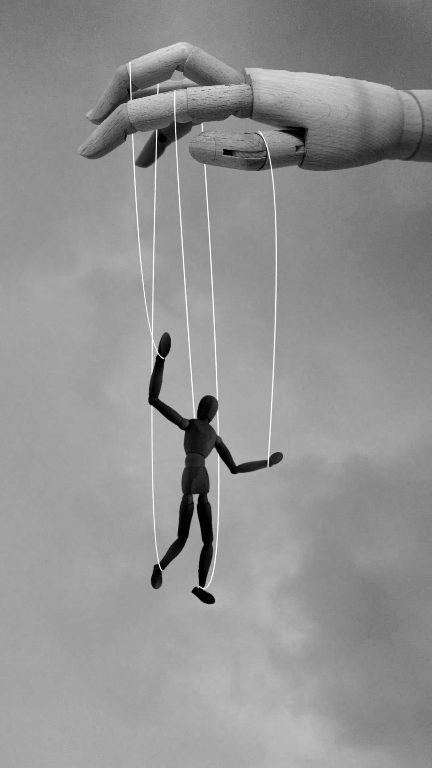 A wooden artist's hand suspending a marionette on strings against an overcast sky