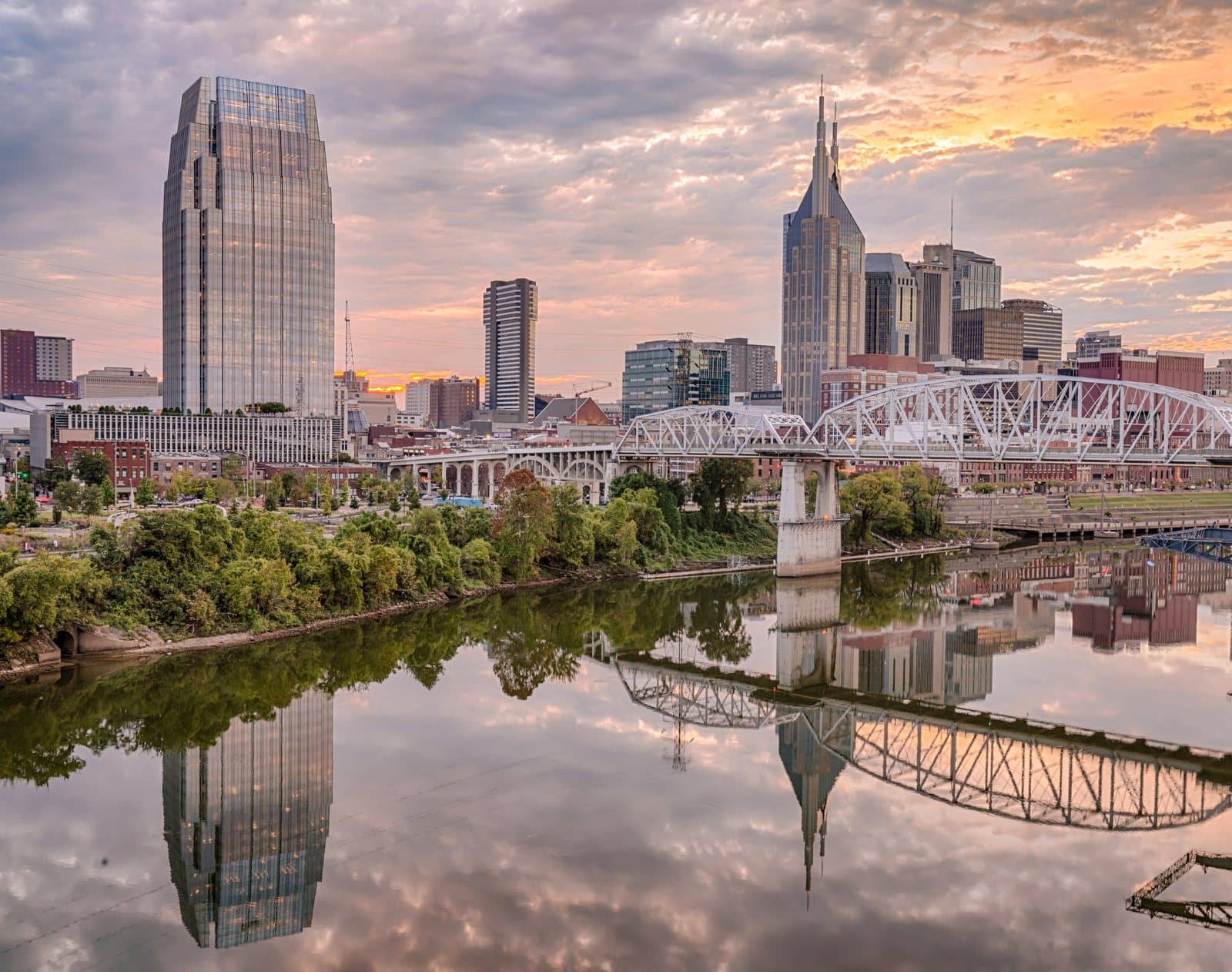 The Nashville skyline at sunset, reflected in the Cumberland River, with the John Seigenthaler pedestrian bridge crossing the water