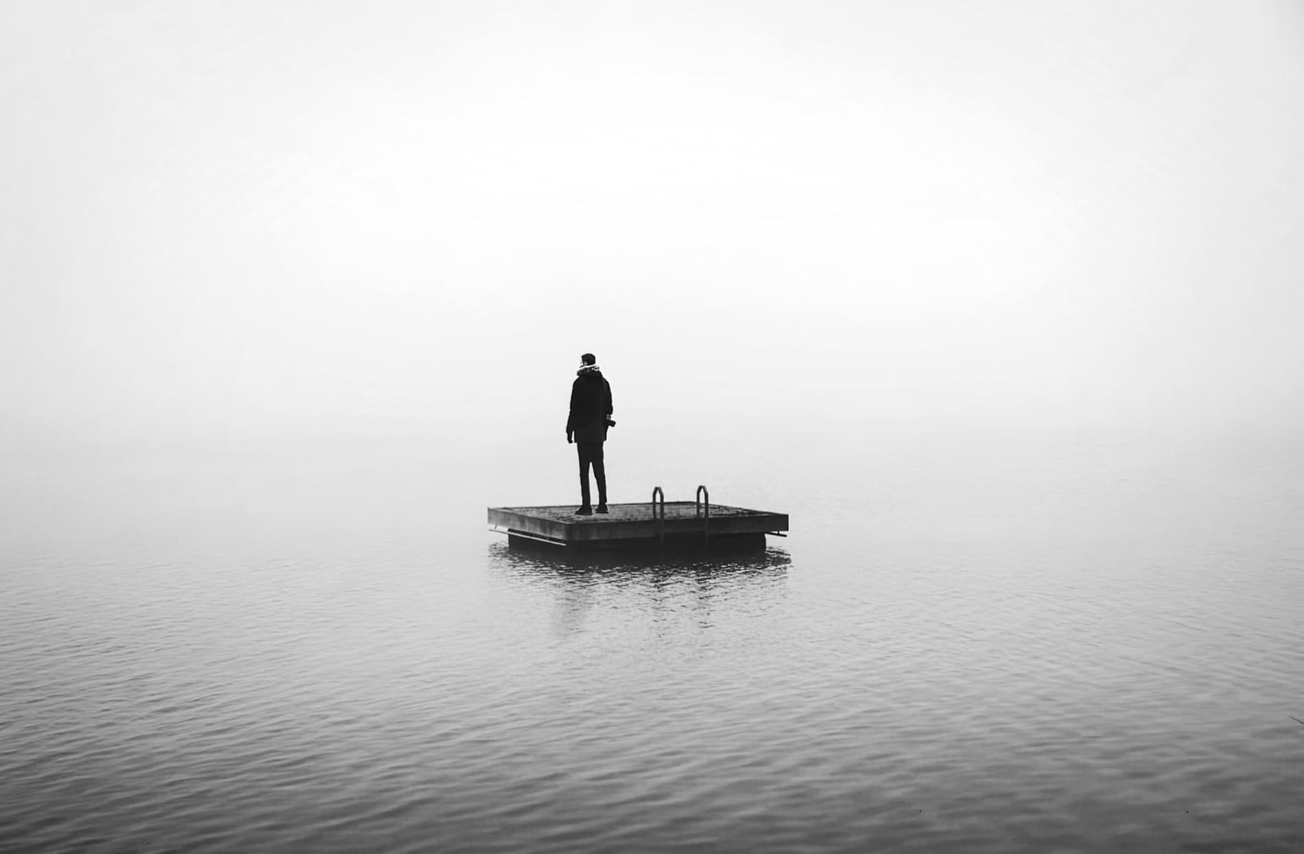 A solitary figure standing on a dock looking out over misty water