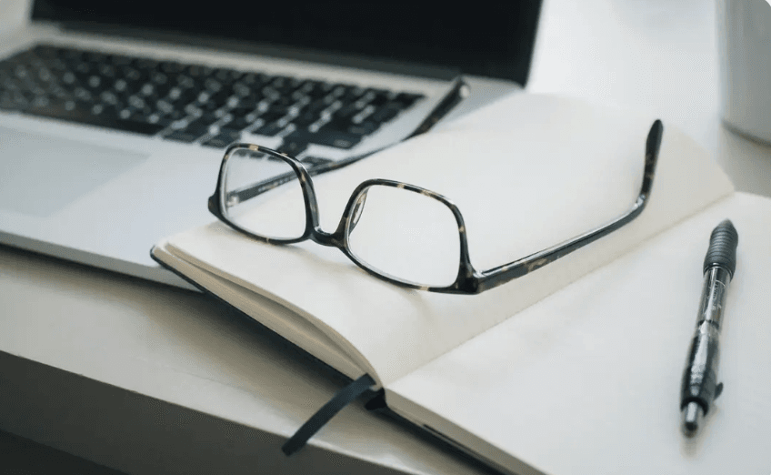 A laptop with reading glasses resting on an open notebook — telehealth therapy