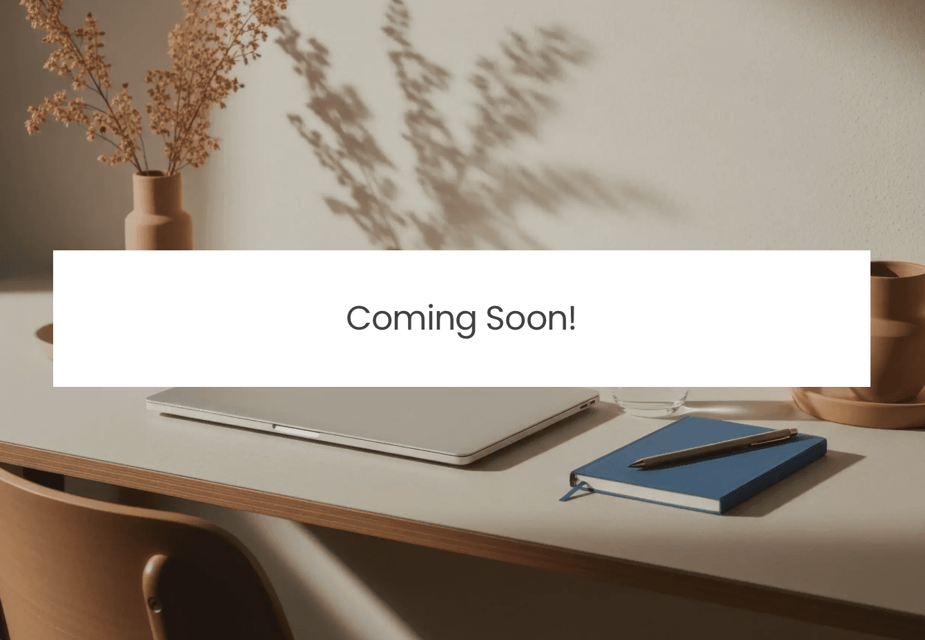 Coming soon — a calm, minimal desk with a closed laptop, a notebook and pen, and a glass of water