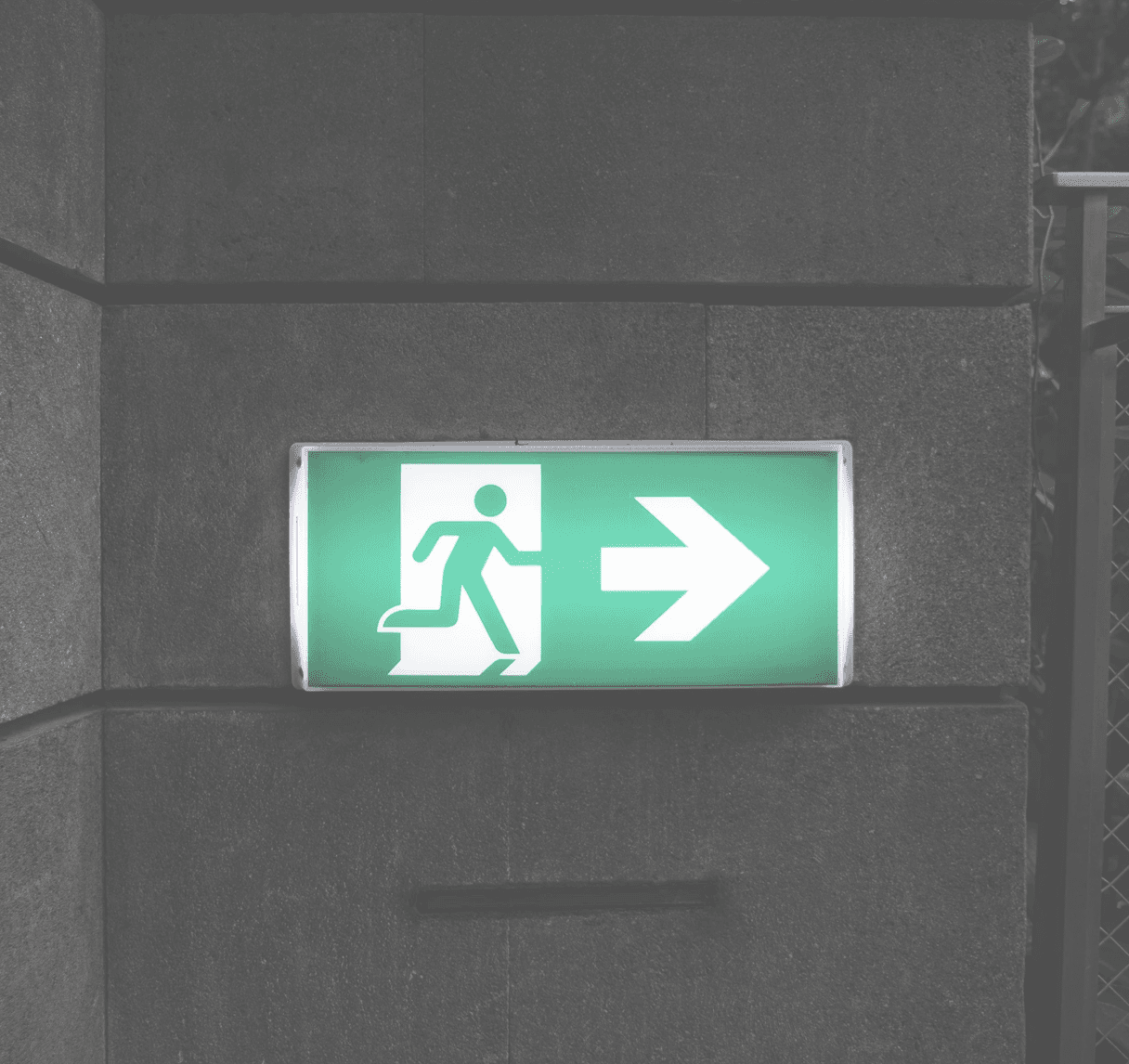 A green exit sign on a stone wall — symbolizing the cost of leaving