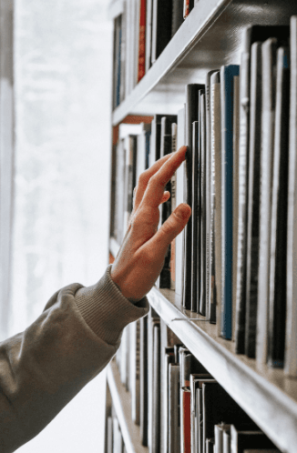 A hand reaching for a book on a sunlit library shelf