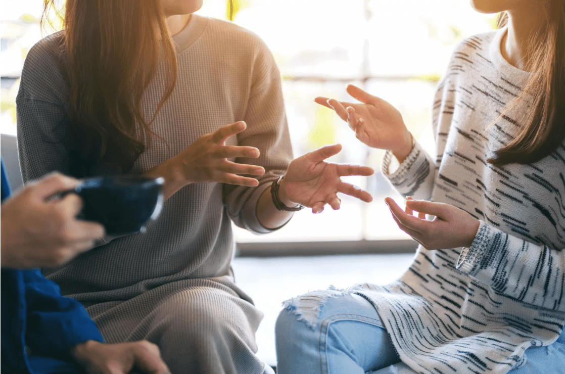 A small group sitting close together in warm window light, hands open mid-conversation — the easy, candid feel of people really talking and listening