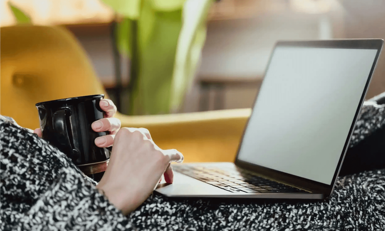 A person reviewing an online workshop on a laptop with a warm cup of coffee