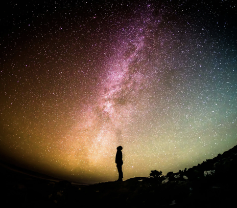 A silhouette of a person standing under a vibrant night sky